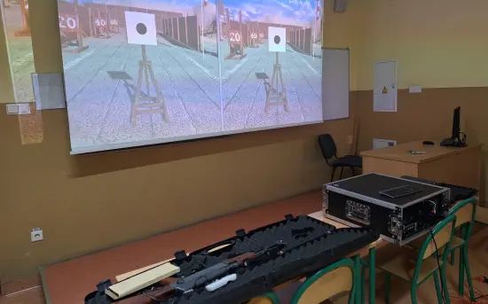 Ekran z rzutnika z tarczami strzeleckimi a przed nimi na stole replika broni długiej